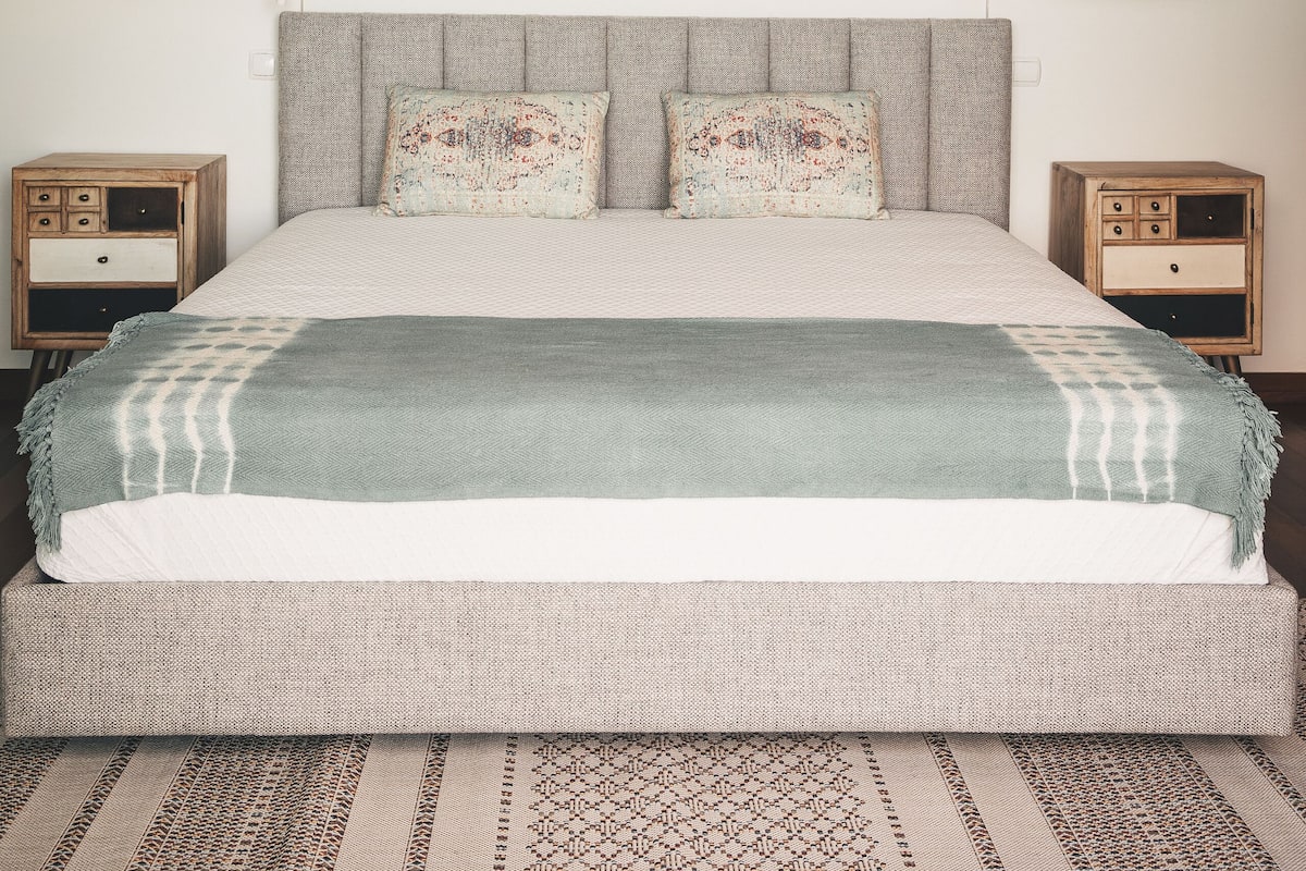 Een slaapkamer met een groot bed, twee nachtkastjes, een spiegel aan de muur en twee hanglampen.