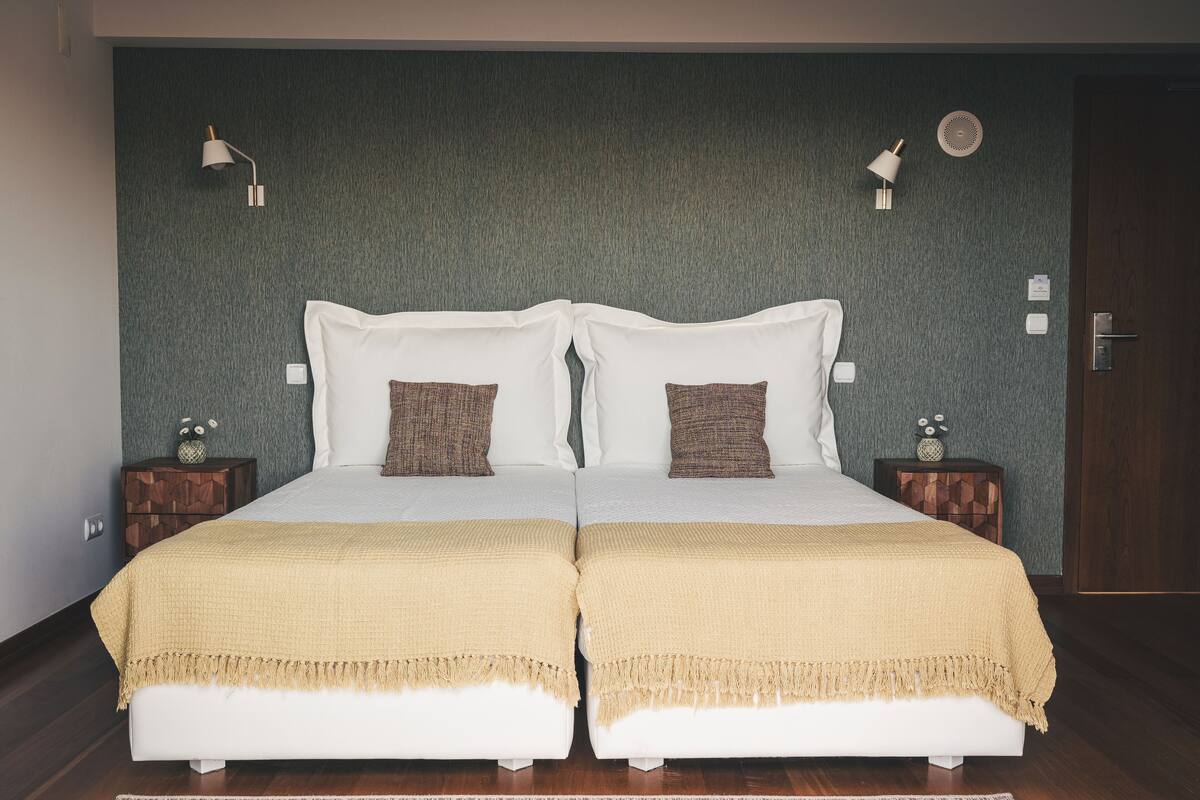 Een tweepersoonsbed met twee kussens, een nachtkastje met een lamp en een wandlamp.