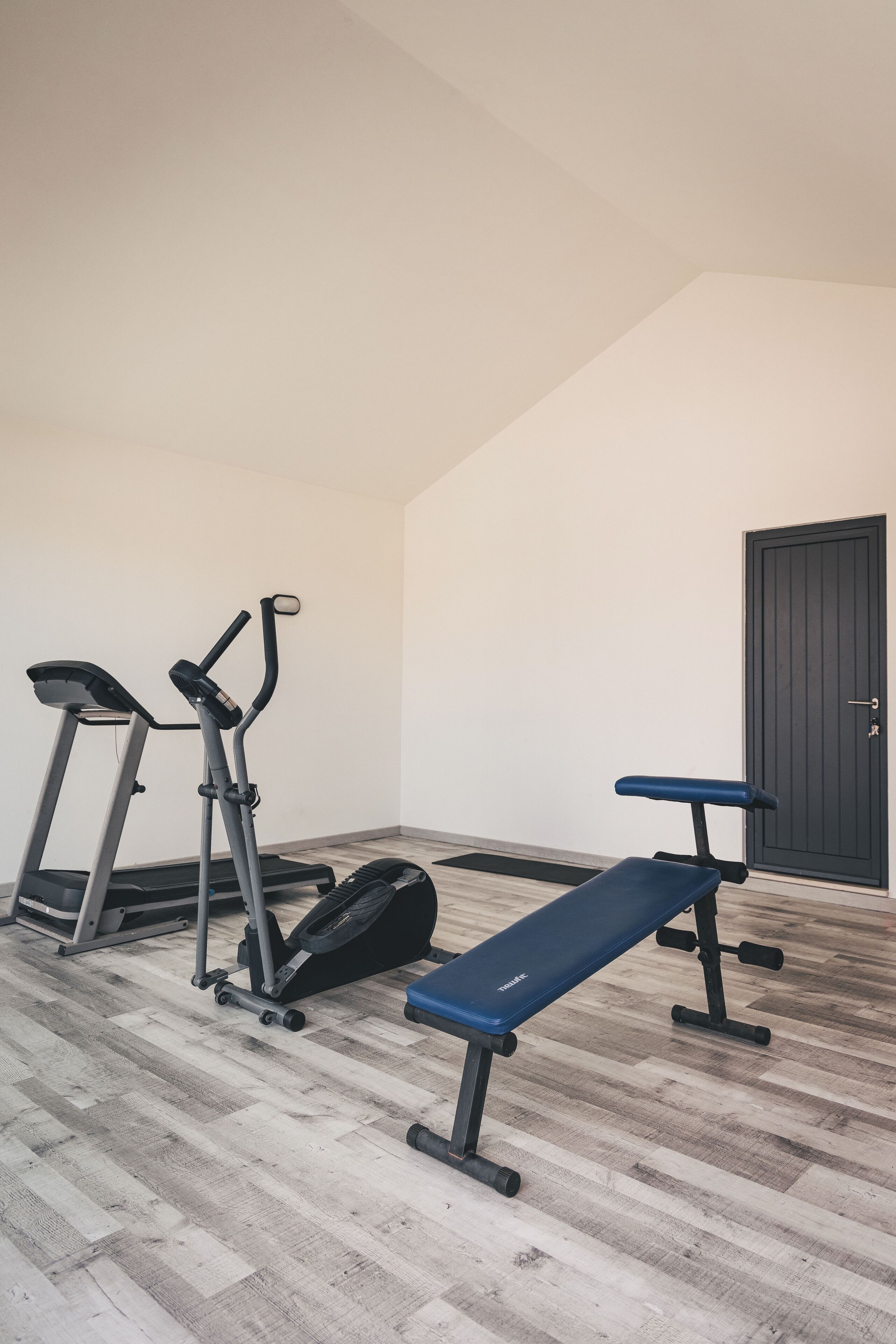A gym with a treadmill, elliptical, and bench.