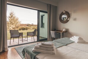 A bedroom with a large sliding glass door leading to an outdoor area, a bed with folded towels, a desk, and a chair. - Vale Pisco (Bombarral)