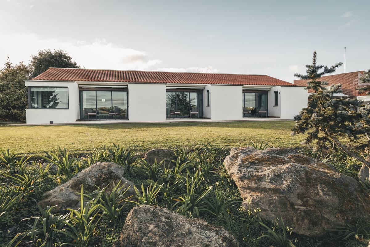 Een modern huis met een rode pannendak, grote ramen en een gazon.