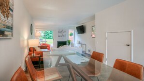 A modern living room with a glass dining table, orange chairs, a sofa, and a fireplace. - Moon River Suites 4 - on River, Private Hot Tub, Downtown NO FLOOD IMPACTS (North Bend)
