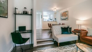 A modern living room with a sofa, a coffee table, and a desk with a chair. There is a staircase leading to another room. - Moon River Suites 4 - on River, Private Hot Tub, Downtown NO FLOOD IMPACTS (North Bend)