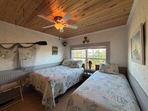 A cozy room with two beds, a ceiling fan, a window with a view, and a wall-mounted lamp.