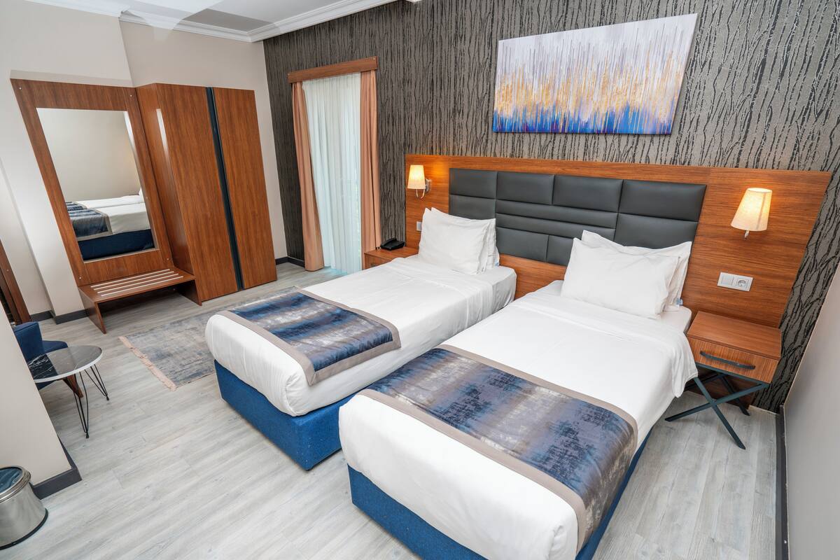 A hotel room with two beds, a desk, a chair, a mirror, and a painting on the wall.