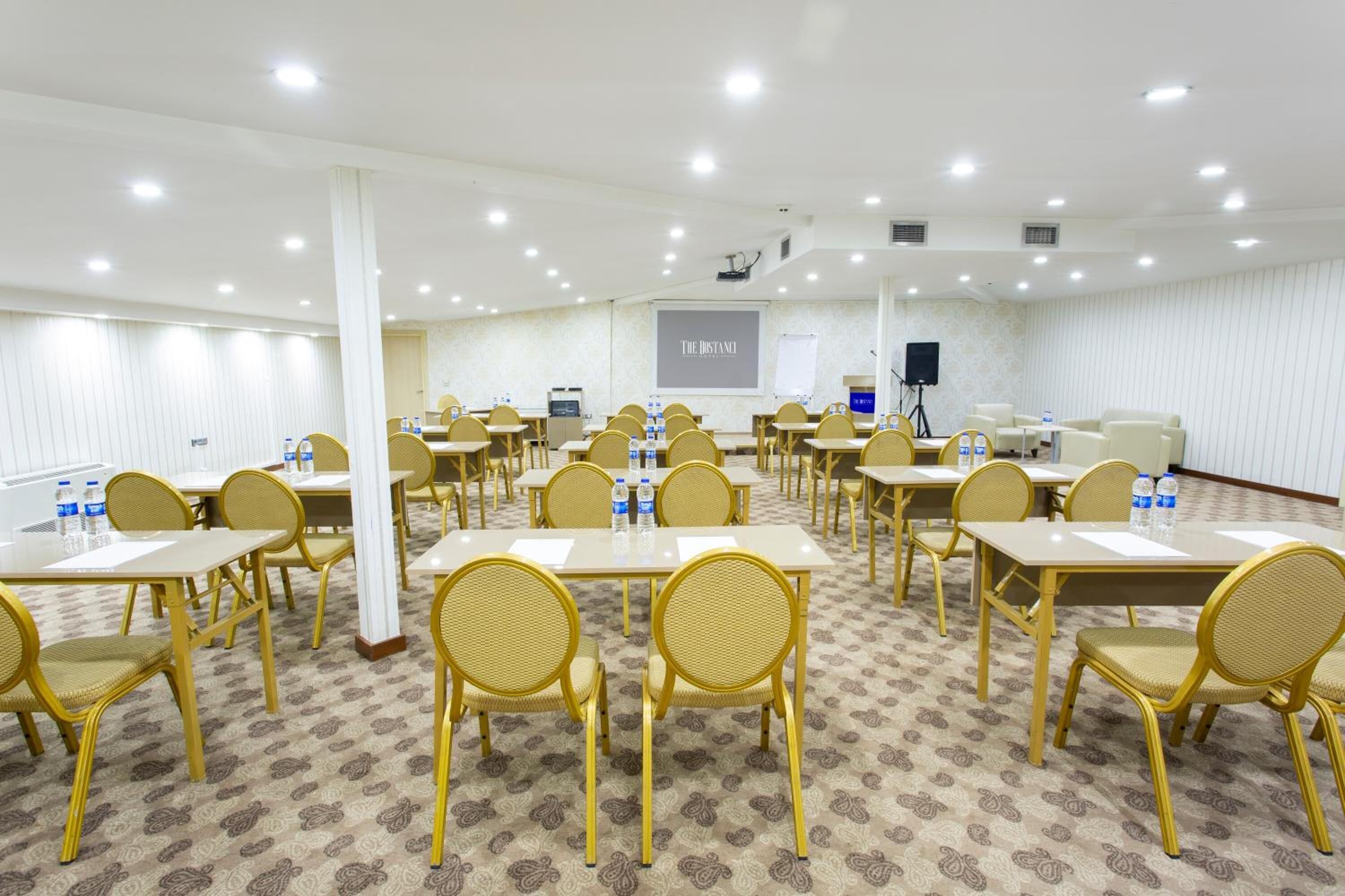 A conference room with multiple tables and chairs, equipped with water bottles, a projector screen, and a whiteboard.