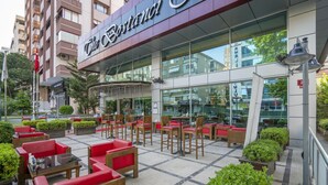 An outdoor seating area with red and wooden furniture, a glass facade, and a sign reading "The Bostanci." - The Bostanci Hotel (Istanbul)