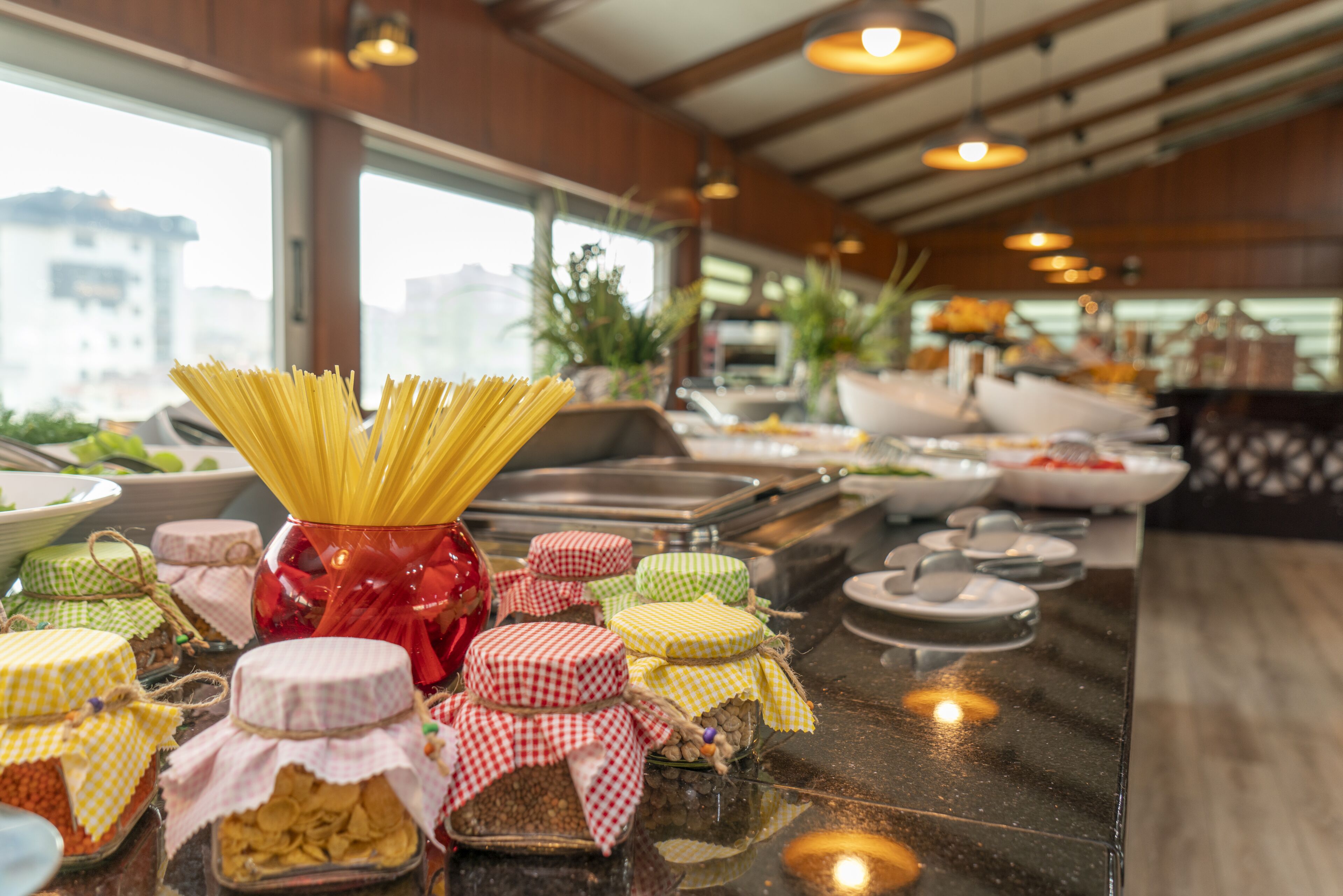 Una mesa de buffet con pasta, diferentes salsas, y frascos de pepinillos y aceitunas.