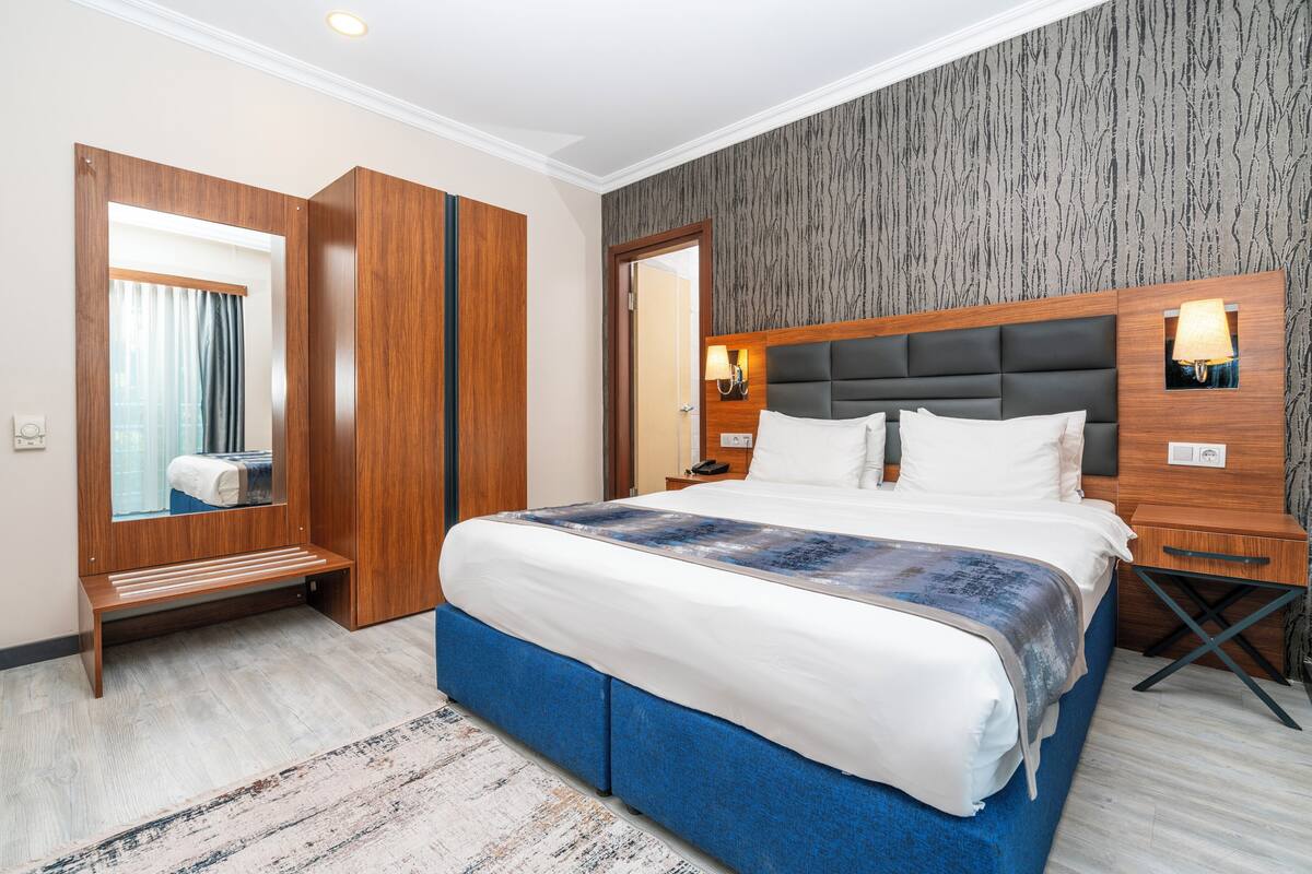 A modern hotel room with a large bed, wooden wardrobe, and a mirror.