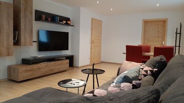 A modern living room with a flat-screen TV, wooden furniture, and a red dining area.