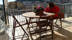 En balkon med et bord og stole, en potteplante og udsigt over bybillede med bygninger og en bakke.