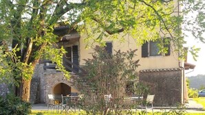 Un bâtiment rustique doté d’une arche en pierre, d’une terrasse et d’un petit arbre en premier plan.