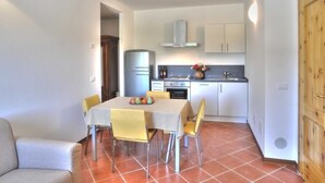 Une cuisine compacte avec des meubles blancs, un four encastré et un petit coin repas agrémenté d’une nappe à carreaux.