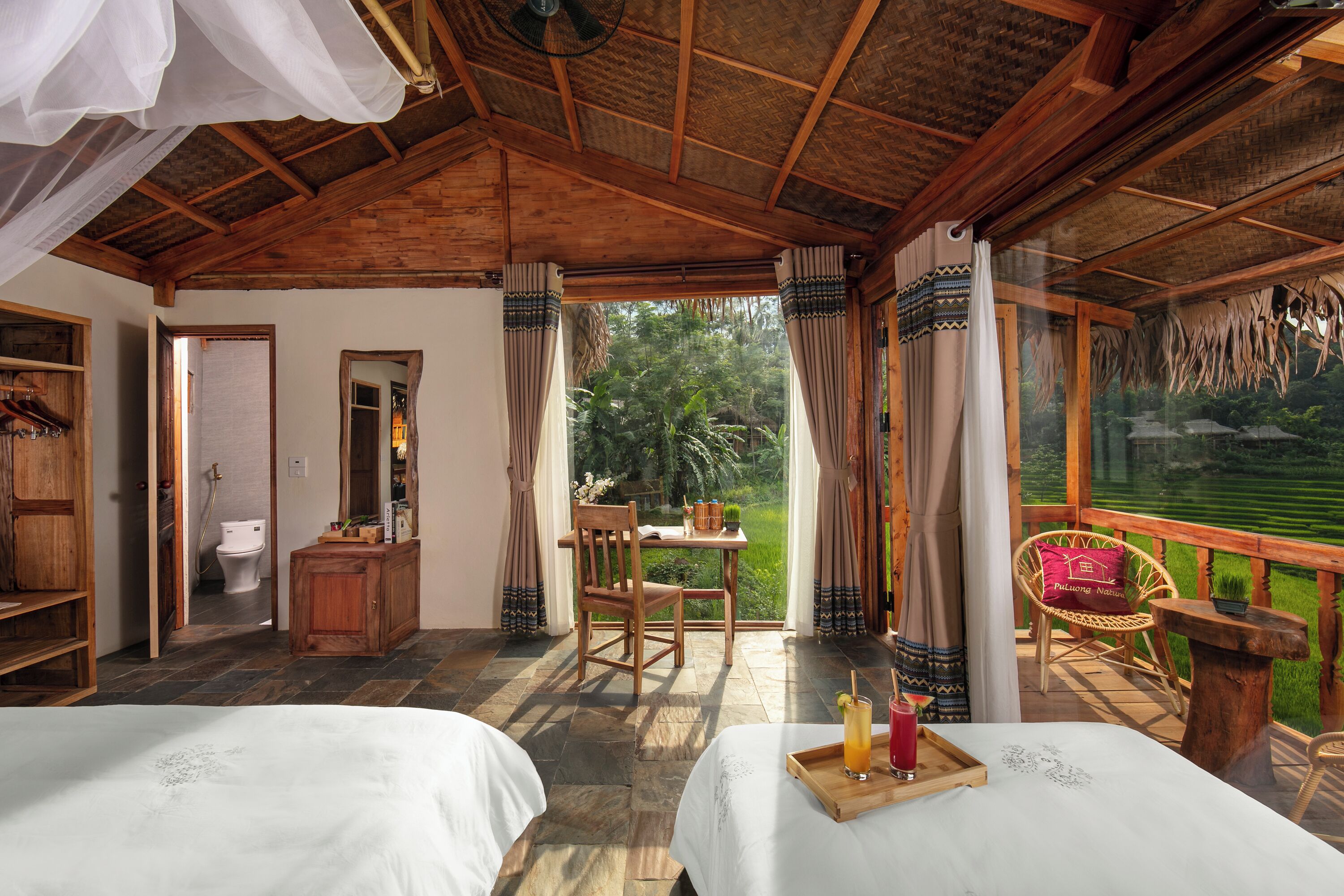Una habitación con dos camas, un escritorio de madera, una silla y vistas a un jardín exuberante.