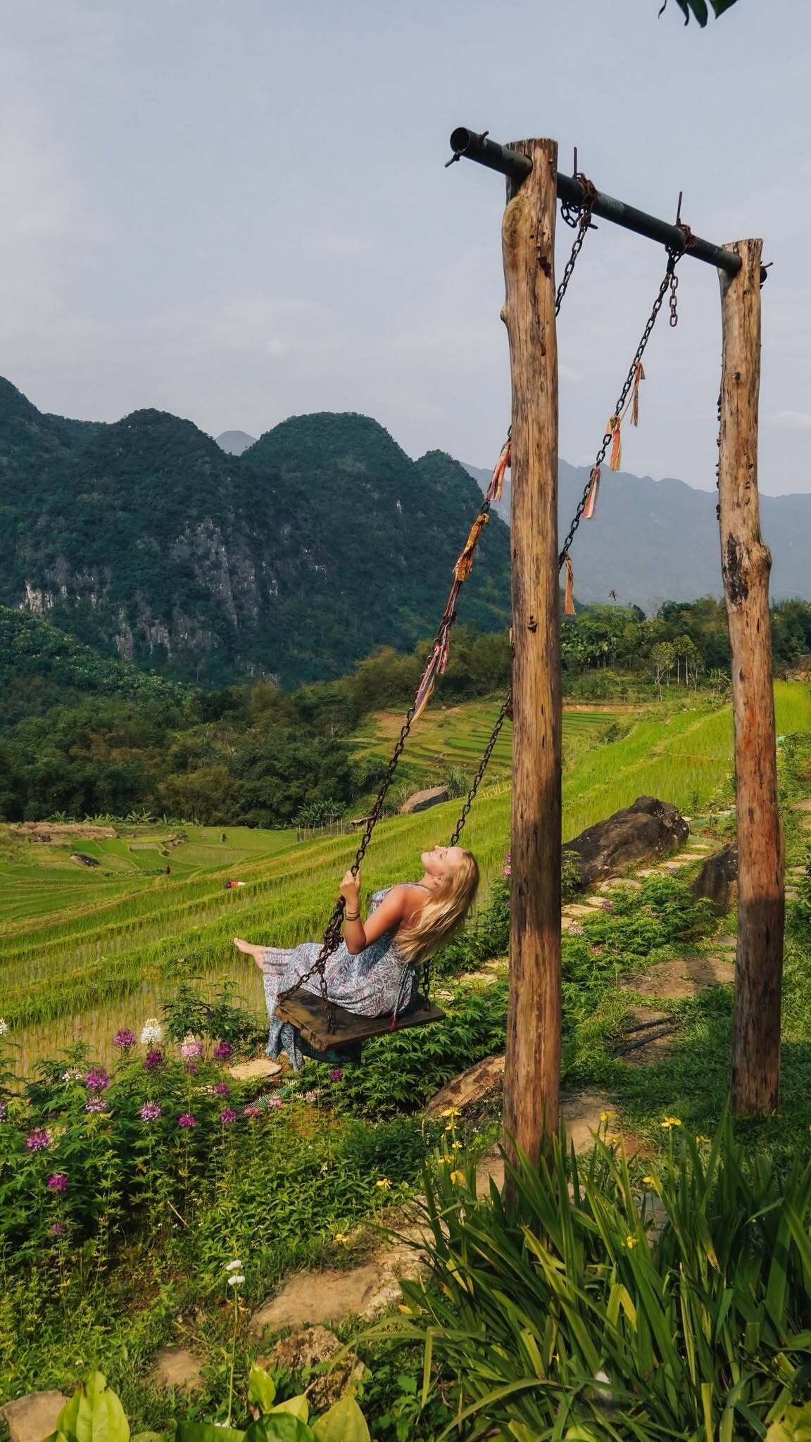 A person on a swing in a rural landscape with mountains in the background.