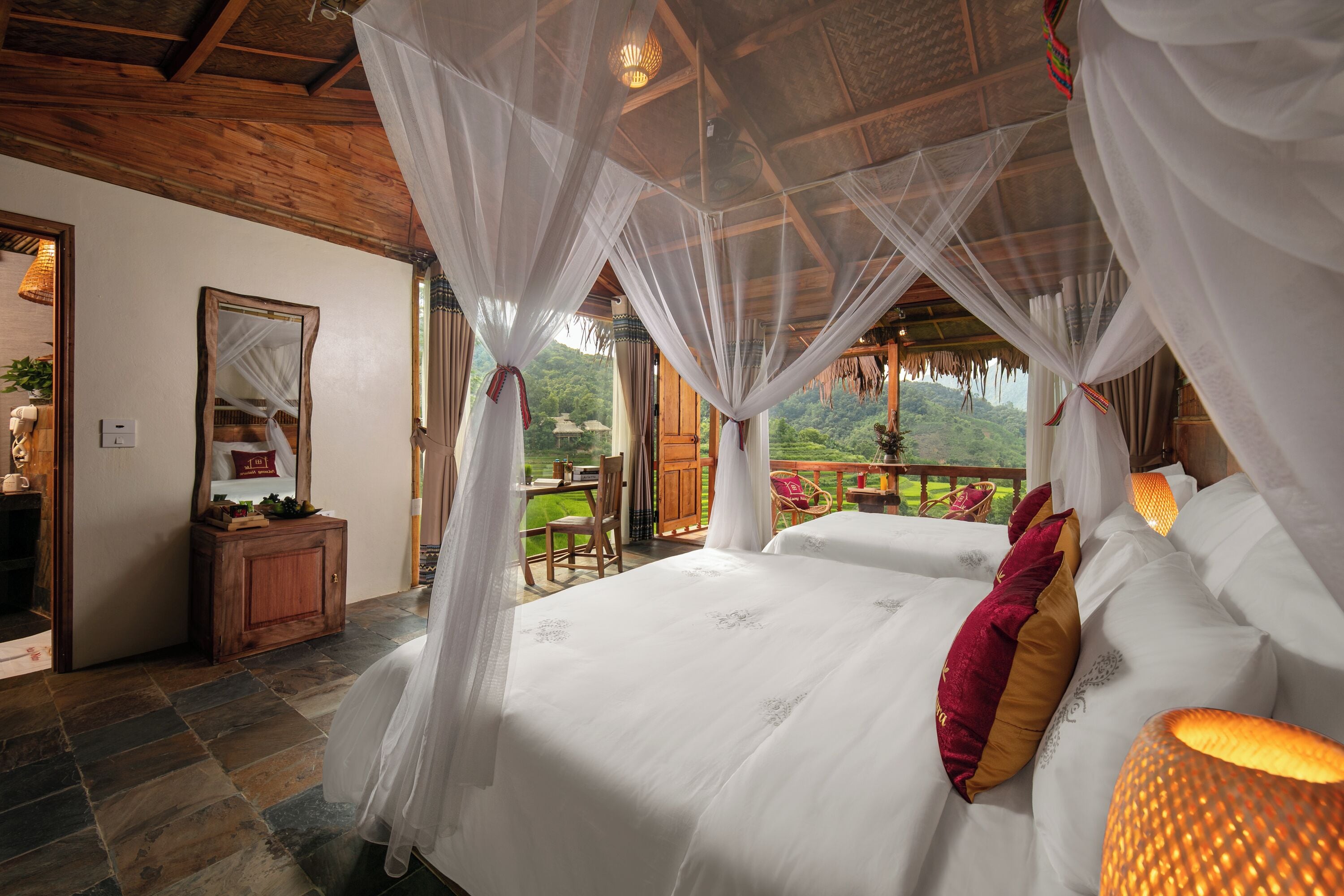 A bedroom with a canopy bed, a wooden desk, and a view of the outdoors.