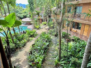 A lush garden with a pool, wooden deck, and a building with a bamboo facade. - Puluong Natura Bungalow (Pu Luong)