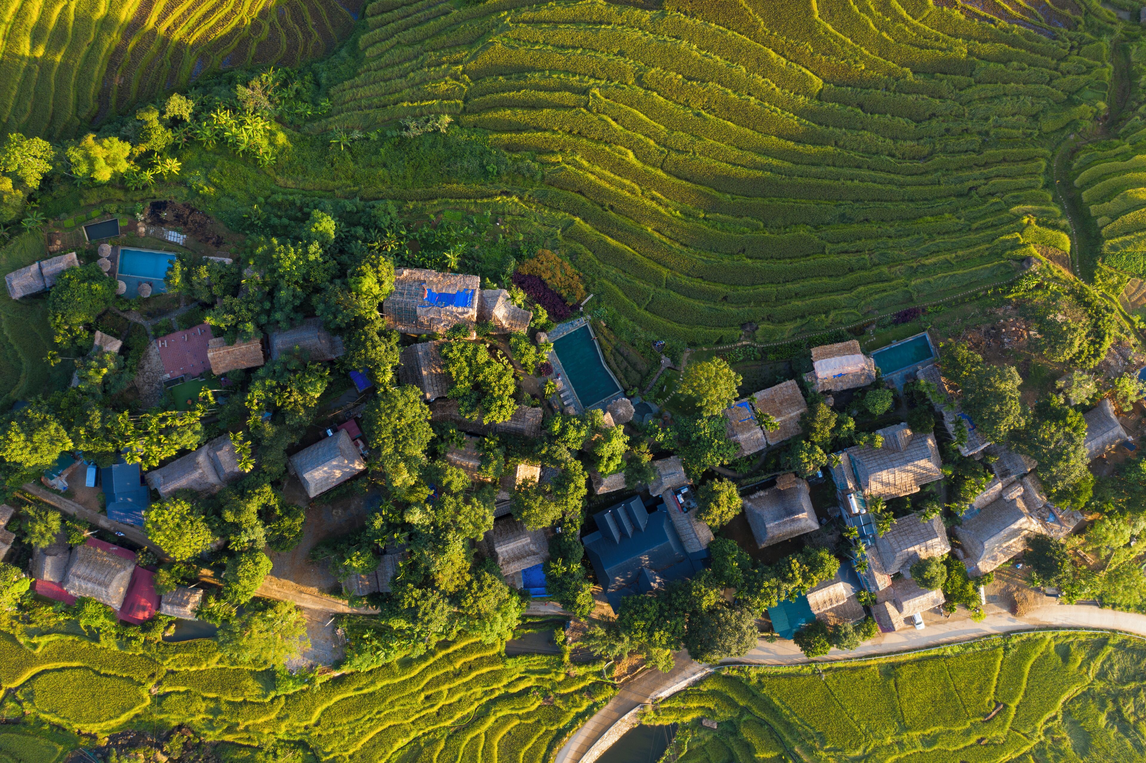 An aerial view of a rural village with terraced fields, traditional houses, and a small bridge.