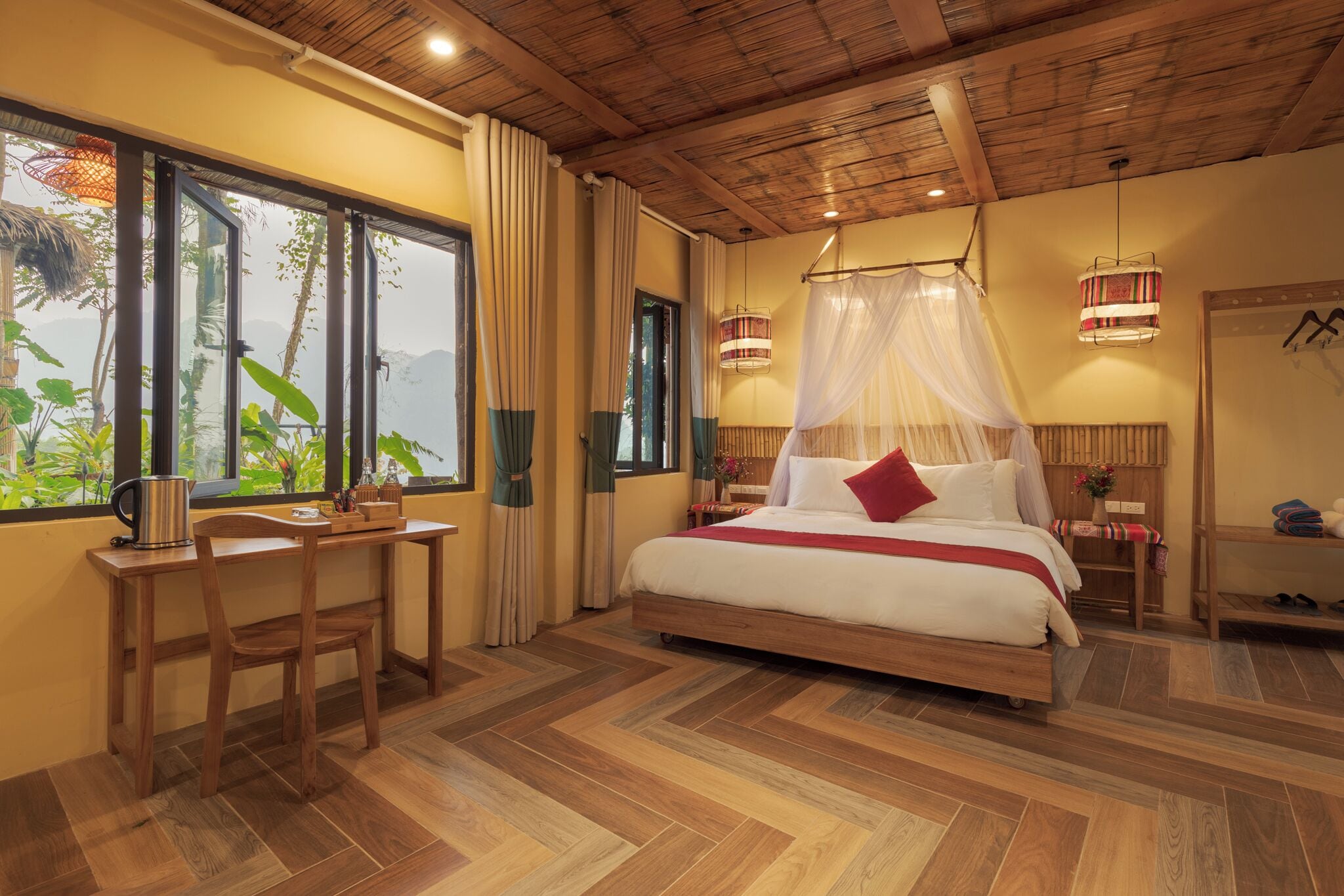 A bedroom with a bed, a desk, and a chair. There is a window with curtains, a bedside table, and a lamp.