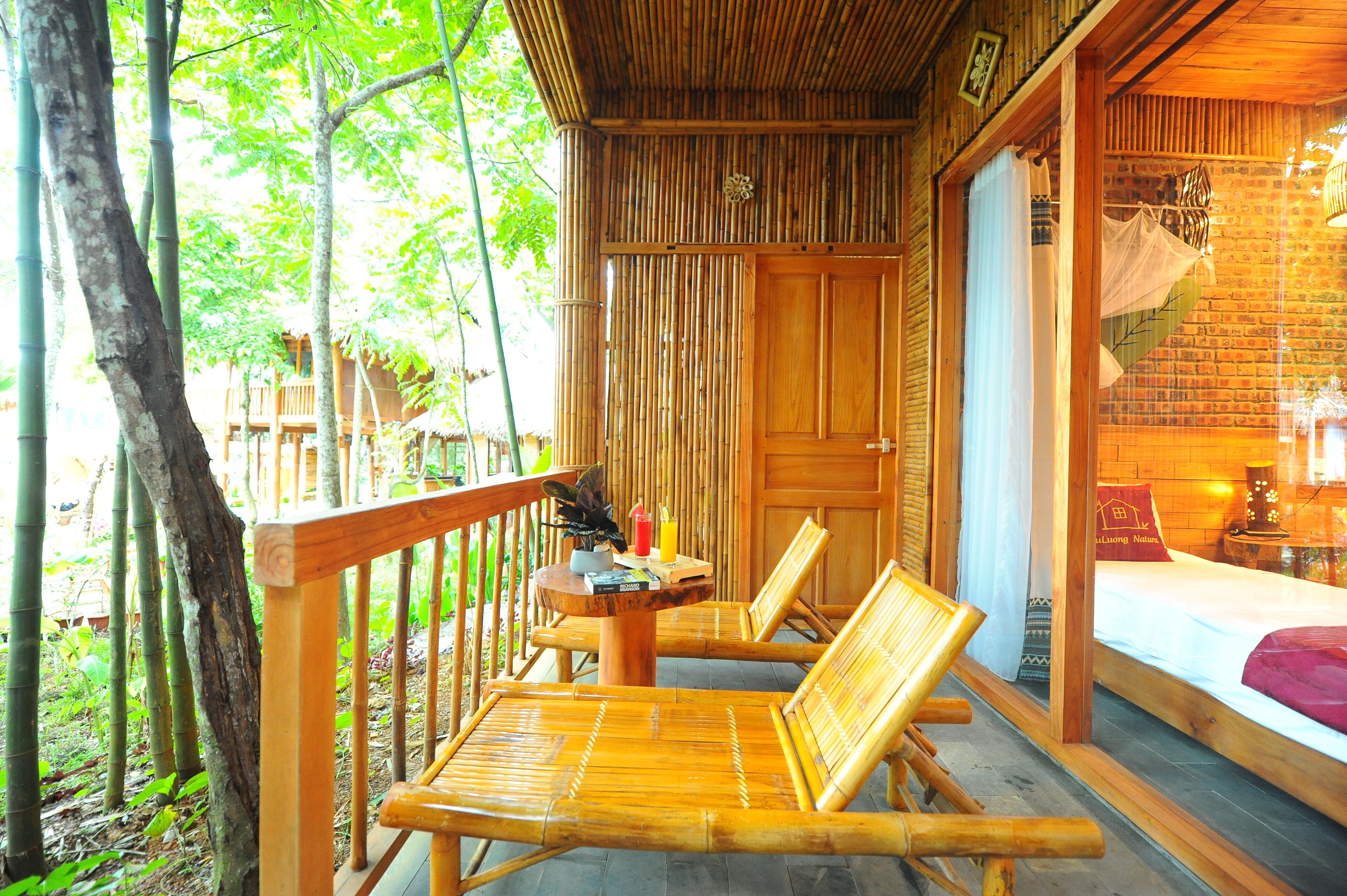 A wooden deck with two bamboo chairs and a table, overlooking a bamboo forest.