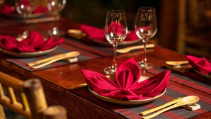 Una mesa de comedor dispuesta con servilletas rojas, cubiertos de madera y copas de vino.