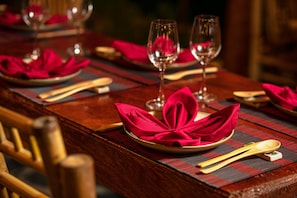 A dining table set with red napkins, wooden cutlery, and wine glasses. - Puluong Natura Bungalow (Pu Luong)