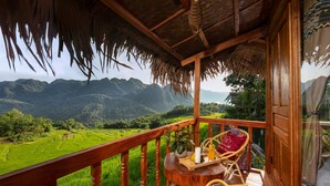 A wooden balcony with wicker chairs, a small table with a tray, and a view of terraced rice fields and mountains. - Puluong Natura Bungalow (Pu Luong)