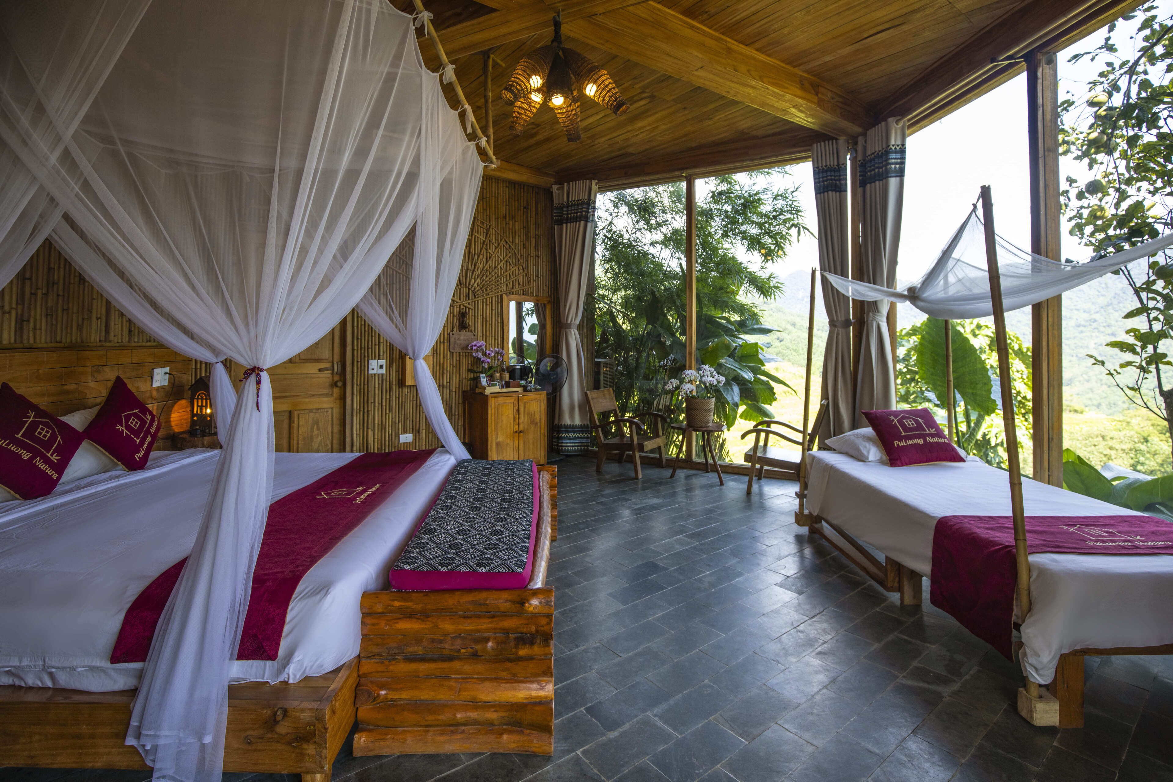 Une chambre avec deux lits, chacun doté d’un baldaquin, d’un plancher en bois et offrant une vue sur la verdure environnante.