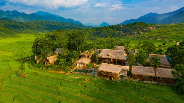 Un pueblo rural con casas tradicionales de techo de paja, rodeado de campos de arroz en terrazas y exuberante vegetación.