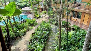 A lush garden with a pool, wooden deck, and a building with a bamboo facade. - Puluong Natura Bungalow (Pu Luong)