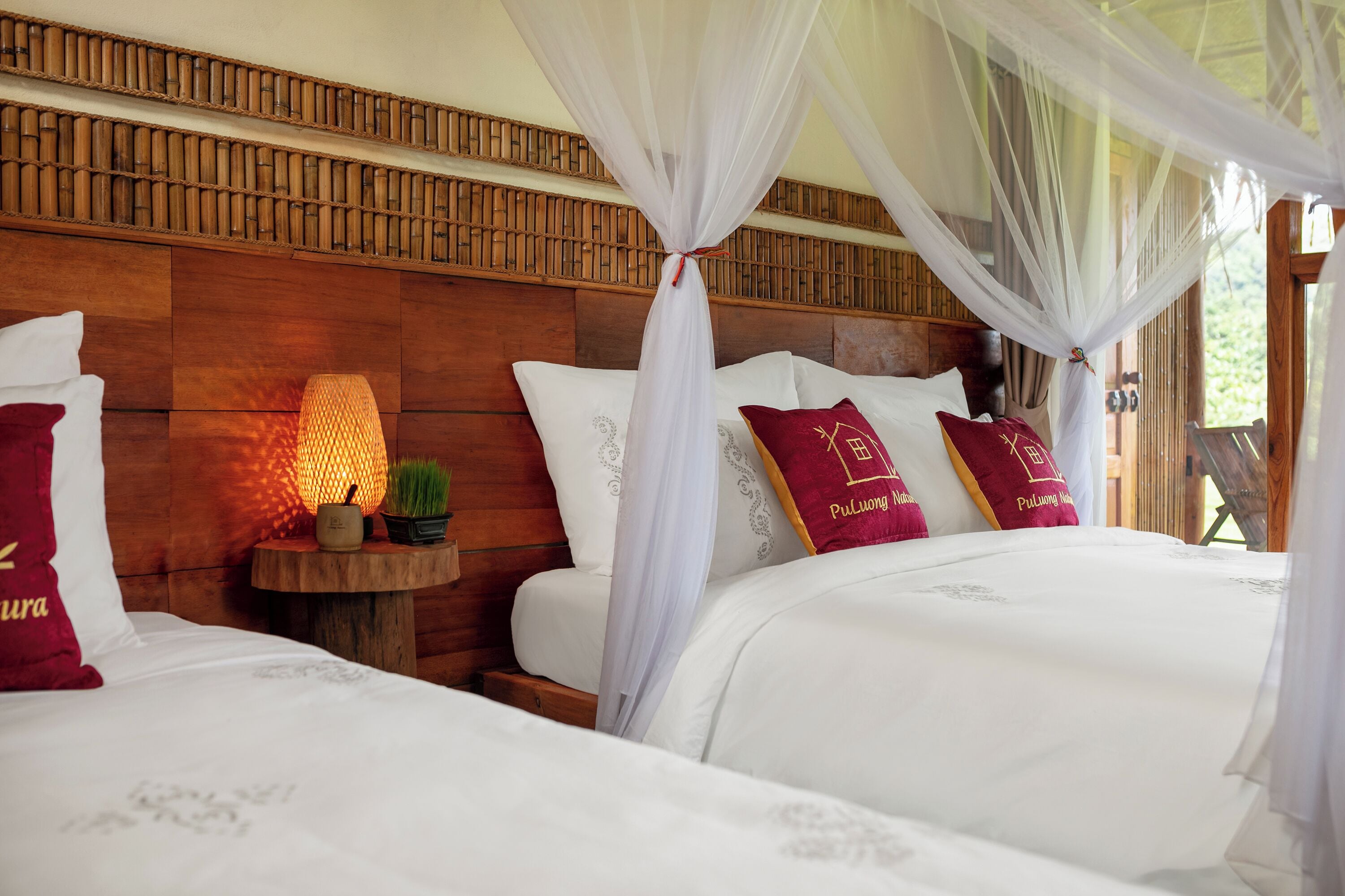 A bedroom with a wooden headboard, white bedding, and a nightstand with a lamp and a small plant.