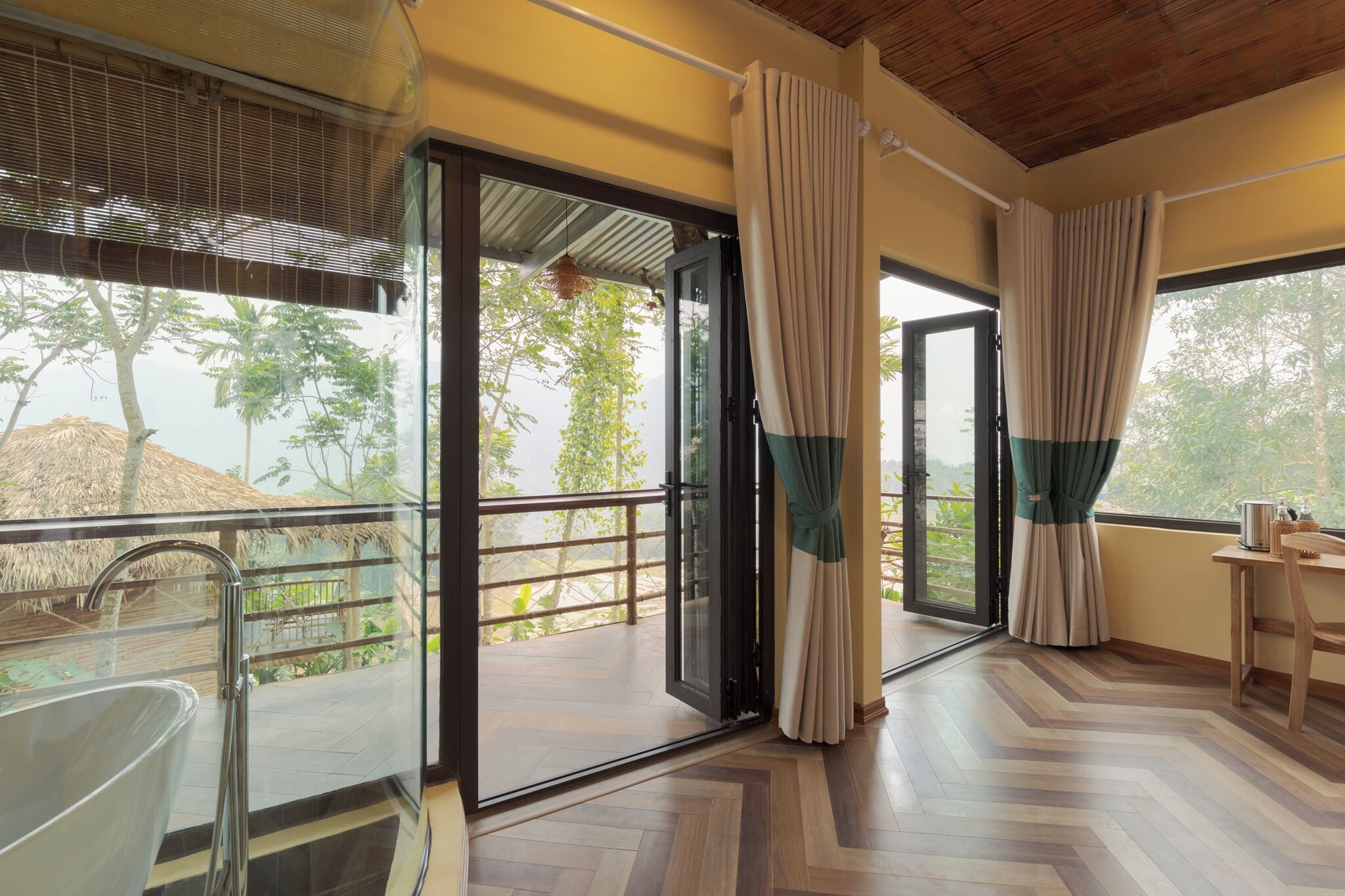 A room with a glass door leading to an outdoor area, a wooden floor, and a table with a chair.