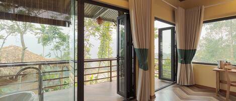 A room with a glass door leading to an outdoor area, a wooden floor, and a table with a chair.