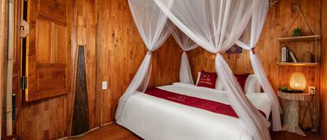 A wooden room with a four-poster bed, a small table with a lamp, and a shelf with books and a plant.