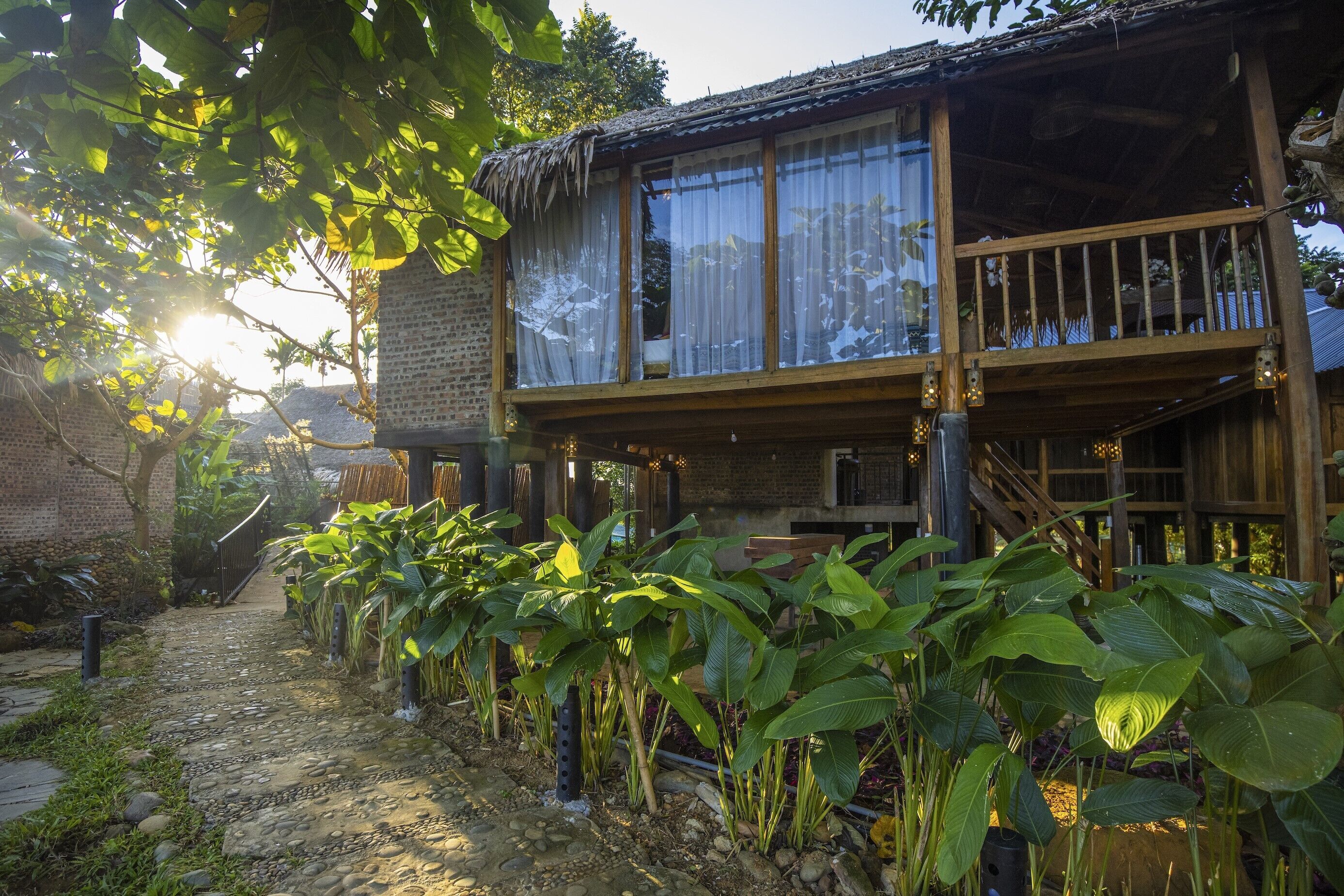 Una casa de madera rústica con balcón, rodeada de abundante vegetación y un camino de adoquinado.