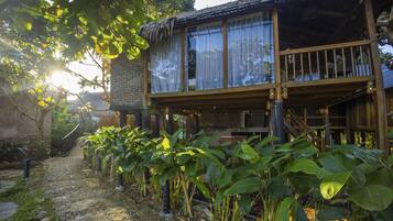 Una casa de madera rústica con balcón, rodeada de abundante vegetación y un camino de adoquinado.
