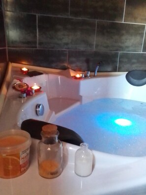 A bathtub with candles, a bottle of orange juice, and a bottle of lotion.