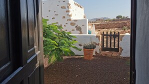 A view through an open door to a courtyard with a white wall, a potted plant, and a black gate. - Villa Cecilio (Puerto del Rosario)