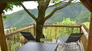 Una terraza de madera con una mesa y sillas, un árbol y vistas a colinas verdes.
