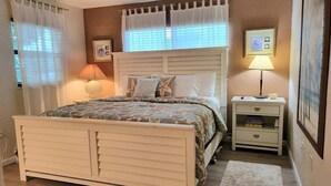 Une chambre à coucher avec un lit, des tables de chevet, une commode, une lampe et un tableau encadré au mur.