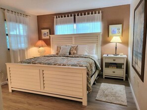 Een slaapkamer met een bed, nachtkastjes, een lamp en een lijst aan de muur.