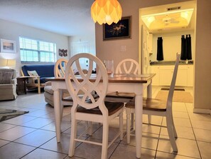 Un comedor con sillas blancas y una mesa de madera, una cocina con armarios blancos y una sala de estar con un sofá y una lámpara.