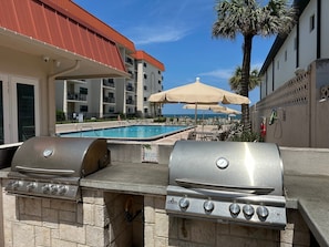 Een buitenzwembad met een barbecue en parasols.