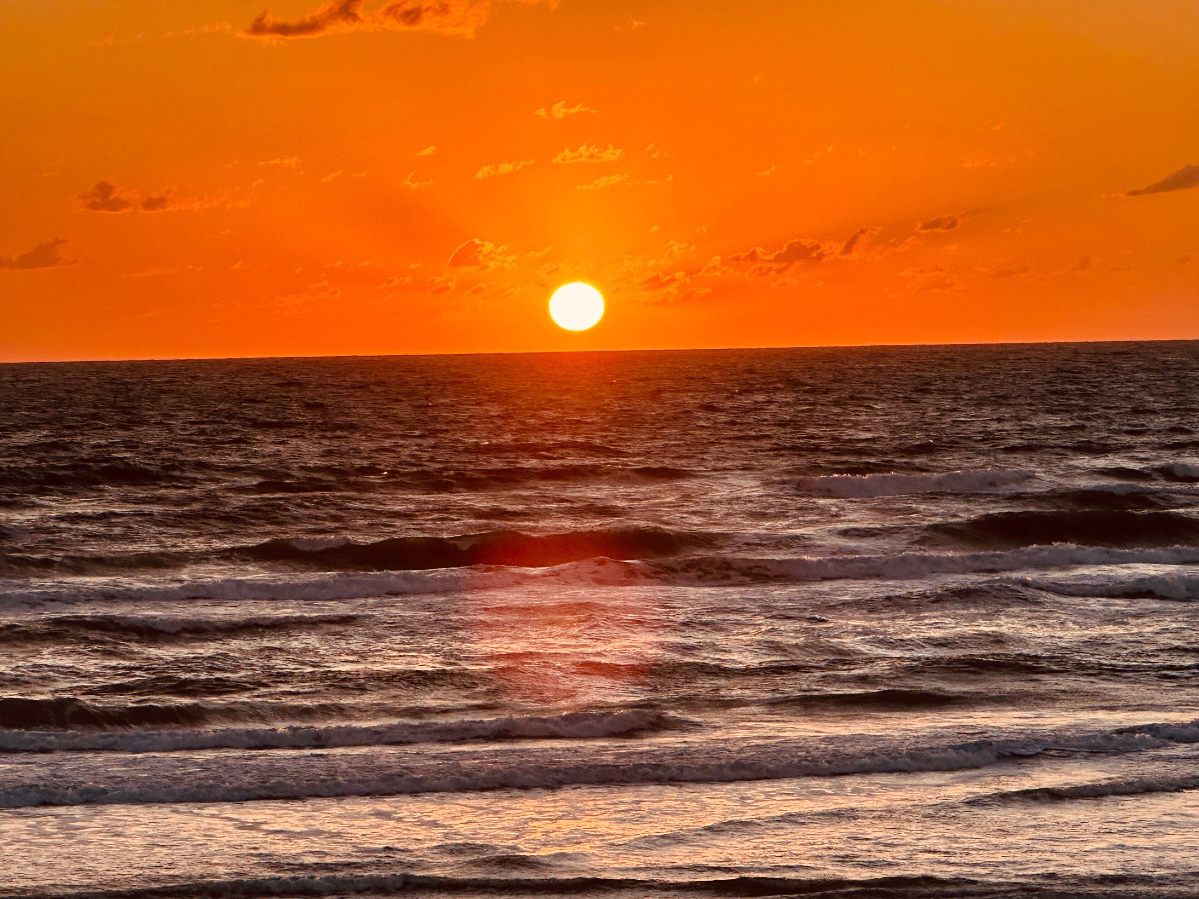 Un coucher de soleil sur l’océan, avec des vagues.