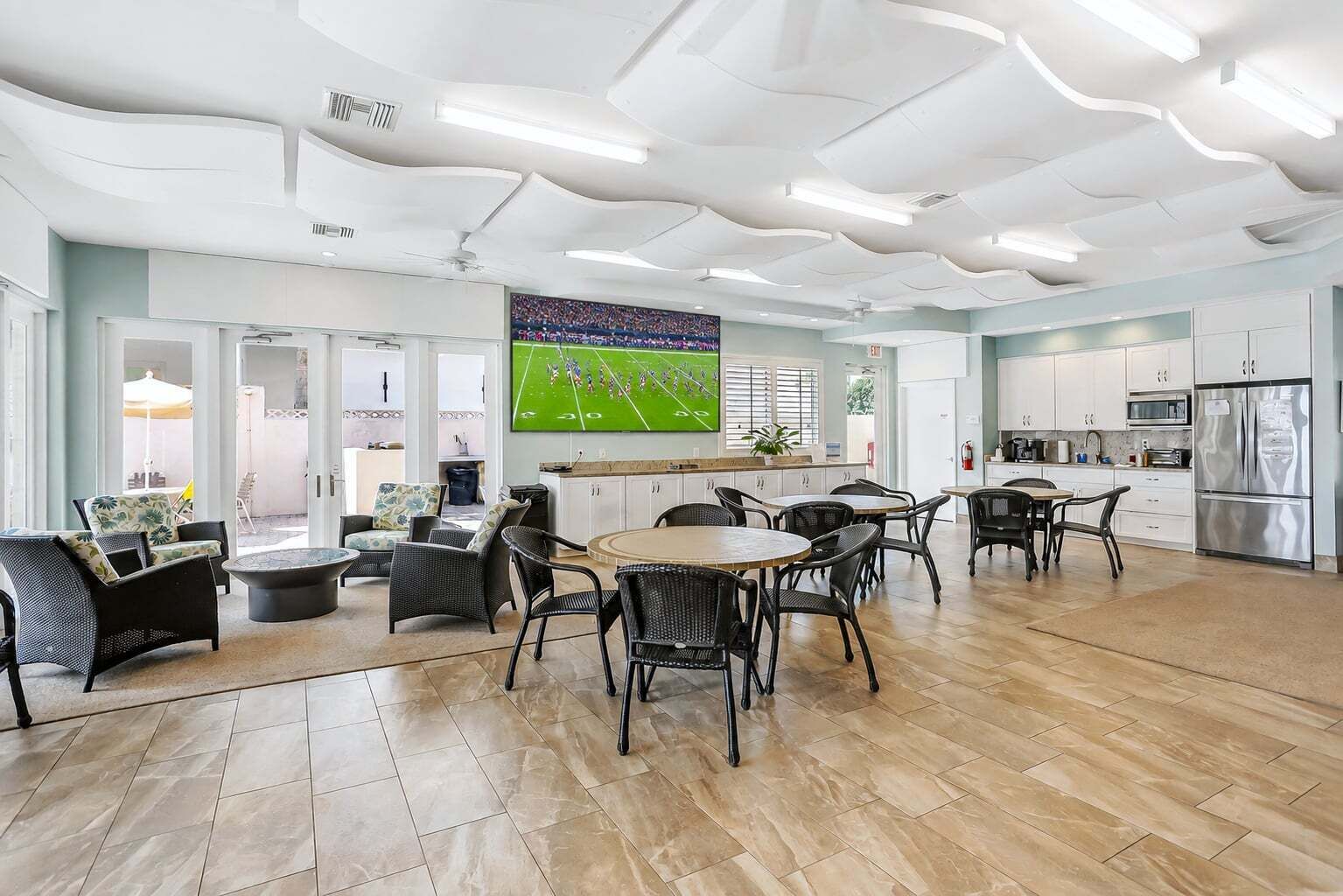 A spacious living area with a large flat-screen TV, a kitchen with modern appliances, and a dining area with wicker furniture.