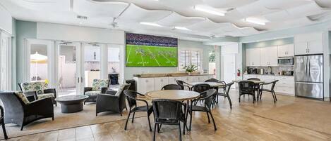 A spacious living area with a large flat-screen TV, a kitchen with modern appliances, and a dining area with wicker furniture.