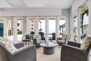 A lounge area with wicker furniture, a central coffee table, and a view of the pool and buildings. - 116 - Oceanfront First-Floor Escape | Steps to the Sand (New Smyrna Beach)