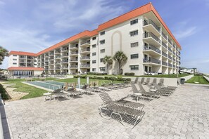 Un hôtel à plusieurs étages doté de balcons, d’une piscine et de chaises longues.