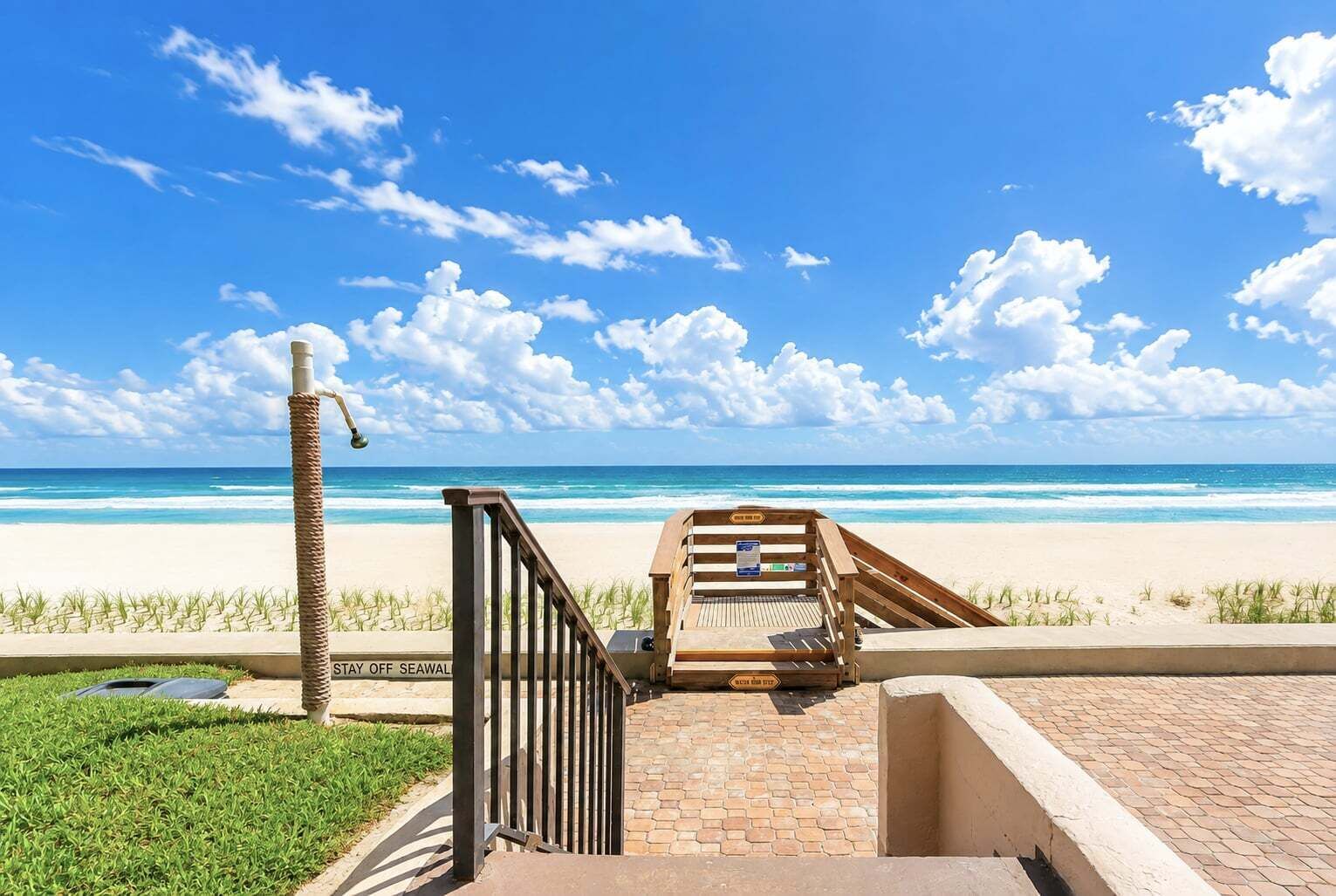 Vista de la playa con una escalera de madera que lleva a una terraza con vista al océano.