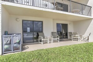 Un balcon avec des chaises blanches, une petite table et un espace abrité équipé d’un barbecue.